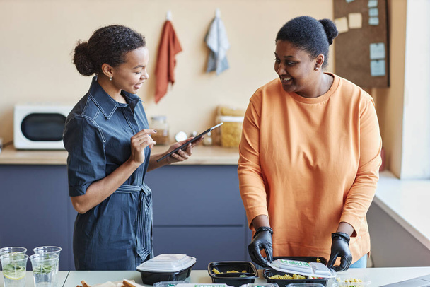 Retrato de cintura hacia arriba de dos mujeres negras revisando pedidos de comida a domicilio en la cafetería y usando tableta, espacio para copiar - Foto, imagen