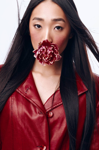 Привлекательная женщина с длинными черными волосами и красной курткой, позирующая с цветком во рту - Фото, изображение