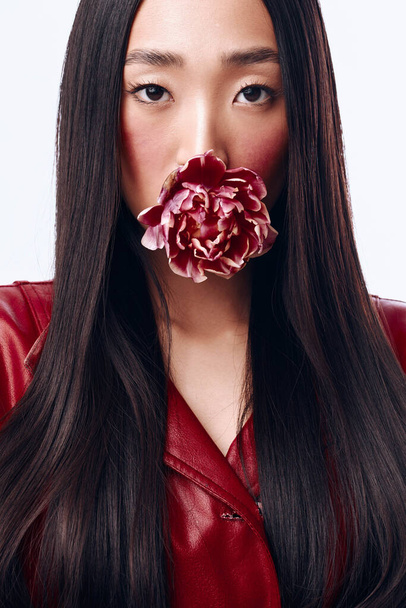 Красива жінка з довгим чорним волоссям позує з квіткою в рот для фотосесії - Фото, зображення