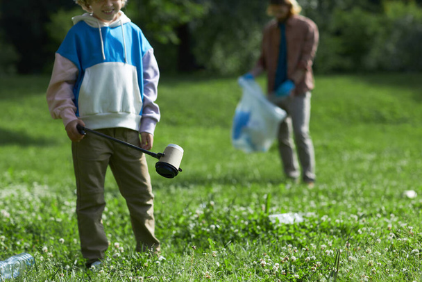 Closeup of little boy picking up trash in nature eco activist family, copy space - Photo, Image