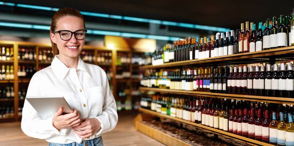 Elinde dijital tabletle kadın perakende müdürü şarap dükkanında duruyor ve gülümsüyor. İş kadını perakende sektöründe çalışıyor. - Fotoğraf, Görsel