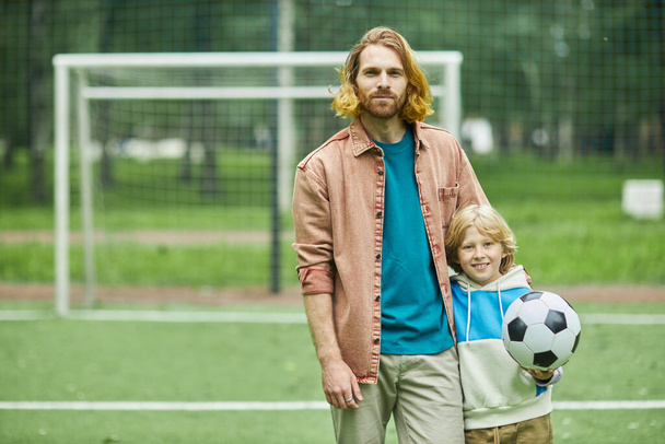 Waist up portrait of young father and son looking at camera outdoors while playing football together, copy space - Photo, Image
