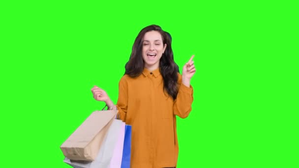 Gelukkige jonge vrouw met kleurrijke tassen na het winkelen, met duimen omhoog op groene geïsoleerde achtergrond. Levensstijl concept - Video