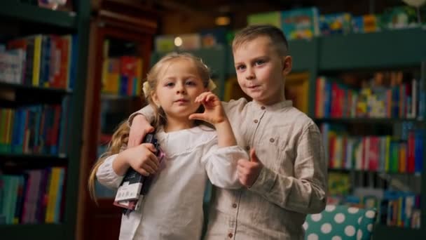 em uma livraria na área de crianças uma linda menina e menino estão abraçando uma foto de família - Filmagem, Vídeo
