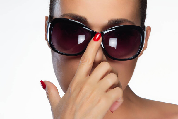 Un hermoso modelo posa con gafas de sol grandes y oscuras y una llamativa manicura roja, aislada sobre un fondo blanco con amplio espacio de copia. - Foto, Imagen