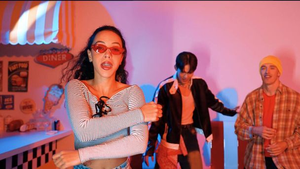 Attraktive kaukasische Tänzerin, die zu Hip-Hop-Musik in die Kamera blickt. Professionelle Tanzgruppen führen im Studio mit rosa LED-Licht energiegeladene Bewegungen und verrückte Schritte auf. Regalisation. - Foto, Bild
