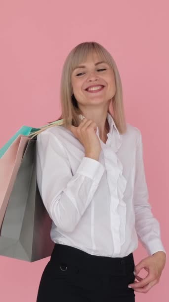 Empresária caucasiana positiva segurando sacos de compras em fundo rosa. Cliente, shopaholic, comprador, conceito do cliente. Vídeo vertical. - Filmagem, Vídeo