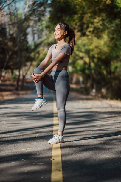 Підходить молода жінка насолоджується сонячним світлом, роблячи стоячу ногу натягнутою, готова до тренування в природній обстановці парку. - Фото, зображення