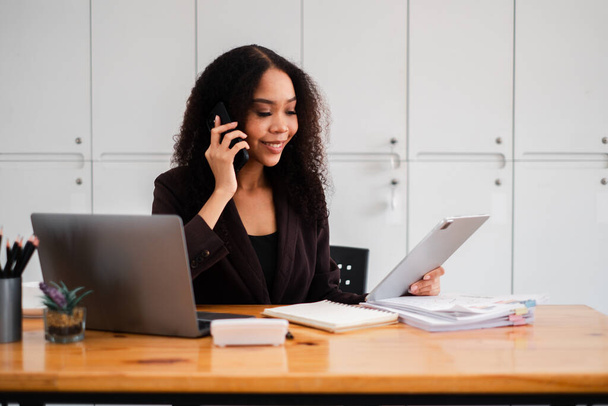 Multitasking da donna d'affari sorridente con una telefonata e scartoffie alla sua scrivania organizzata con un computer portatile. - Foto, immagini