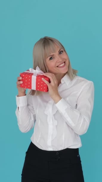 Φιλική και περίεργη Καυκάσια επιχειρηματίας λαμβάνει κουτί δώρου σε μπλε φόντο. Εκτίμηση, συγχαρητήρια, γιορτή. Κάθετη βίντεο. - Πλάνα, βίντεο