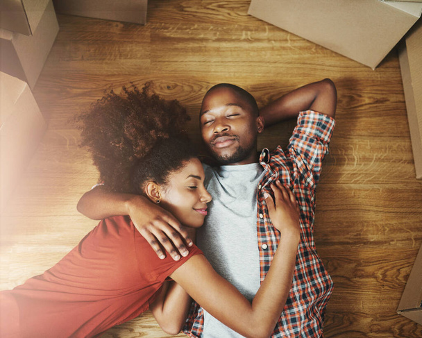 Sleep, moving and black couple on floor in new home with boxes, tired hug and mortgage with high angle. Relax, man and woman in house with romantic embrace with love property investment and fatigue. - Photo, Image