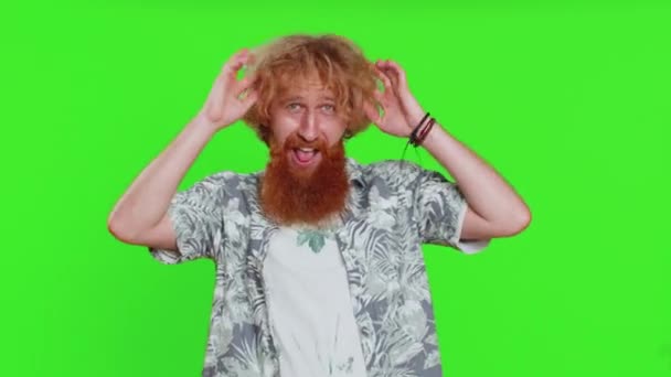 Веселий комічний грайливий молодий бородатий чоловік робить дурні вирази обличчя і похмурість, обдурюючи, показуючи язик, ідіотичний вираз. Хлопець ізольований на фоні ключа зеленої хроми. Люди стиль життя - Кадри, відео
