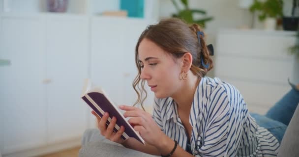 Een ijverige vrouwelijke student houdt zich bezig met gericht leren en studeren, geabsorbeerd in het lezen van een boek in het comfort van haar thuisomgeving - Video