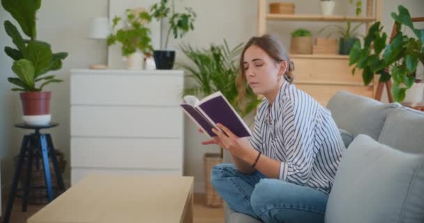 Een vrouw draagt een glimlach als ze in de verte kijkt, verdwaald in dagdromen terwijl ze een boek vasthoudt, vreugdevolle mijmering mengend met het plezier van het lezen - Video