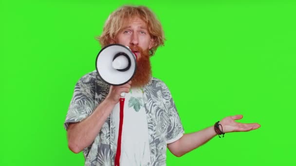 Happy caucasian man talking with megaphone, proclaiming news, loudly announcing advertisement discounts sale, using loudspeaker to shout speech. Redhead guy isolated on green chroma key background - Footage, Video