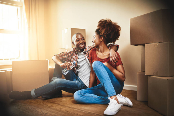 Black couple, real estate and embrace on floor of new house with bonding, support and break from moving day. People, homeowner and excited for property investment, dream home or relocation with boxes. - Photo, Image