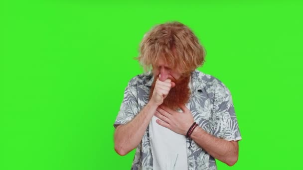 Unhealthy young caucasian man coughing with seasonal flu symptoms covering mouth with hand, feeling sick, allergy, fever or viral infection. Unwell ill guy isolated on green chroma key background - Footage, Video