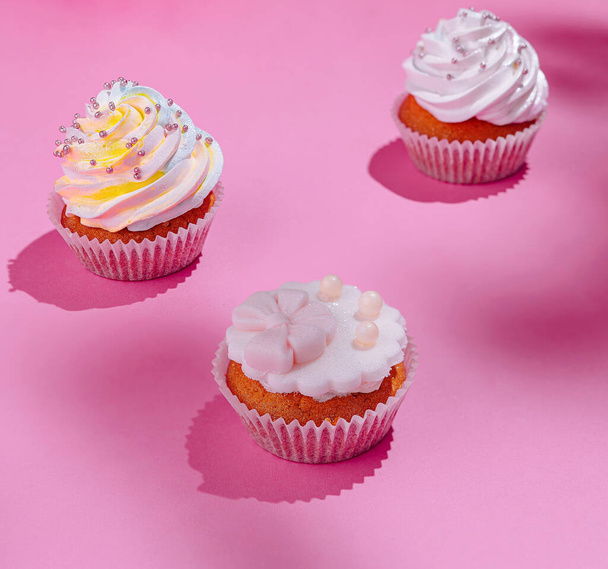 Elegante Cupcakes mit weißem Zuckerguss und Dekorationen vor lebendigem rosa Hintergrund - Foto, Bild