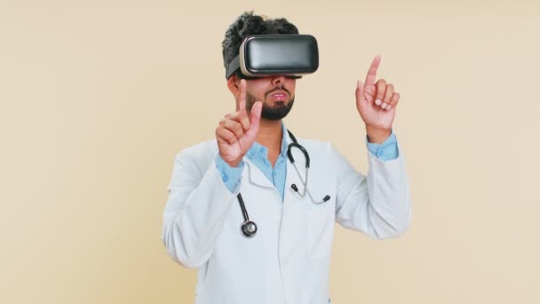 Heyecanlı Hintli doktor kardiyolog kulaklık uygulaması kullanarak sanal gerçeklik 360 videosu izliyor. VR gözlüklü, bej arka planda Arap eczacı. Geleceğin tıp teknolojisi. - Video, Çekim