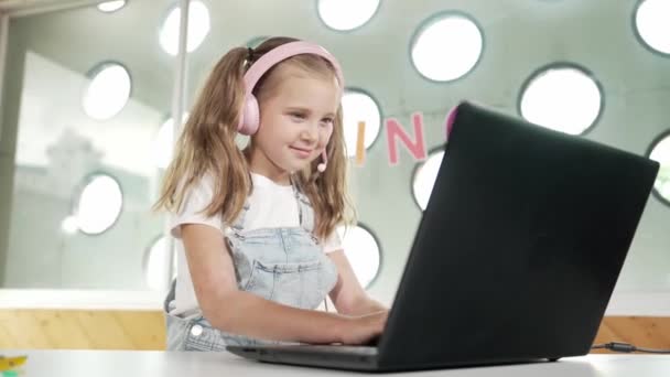 Jonge student die werkt op een laptop of studeert in een online klas. Blank meisje typen op laptop tijdens het doen van huiswerk of het luisteren muziek.Little kind dragen hoofdtelefoon. Creatief leren. Erutie. - Video