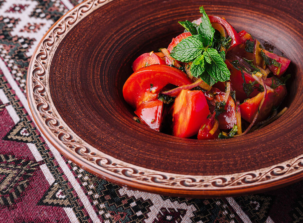 Lebendiger georgischer Salat in einer Tonschale, garniert mit frischen Kräutern, auf einer ethnischen Tischdecke - Foto, Bild