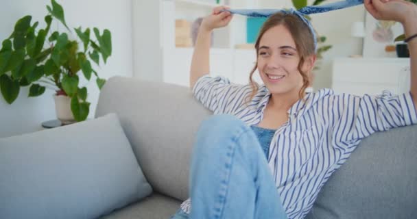 Een glimlachende vrouw zit op de bank, haar uitdrukking gevuld met geluk en vreugde als ze zich overgeeft aan dagdromen, verloren in gedachten van geluk en positiviteit - Video