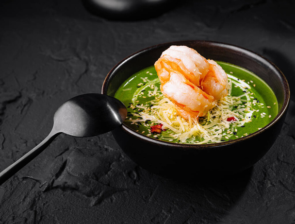 Gourmet bemutatása garnélarák spenótleves díszített öntetek egy sötét tál egy texturált felületen - Fotó, kép