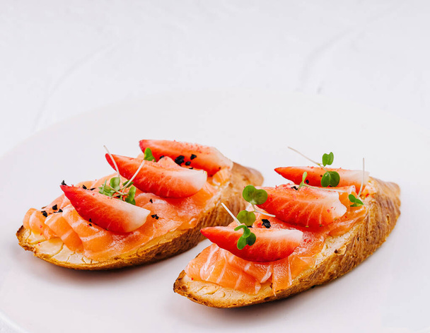 Елегантні копчені тости лосося, прикрашені свіжими травами та скибочками полуниці, подаються на чистому білому тлі - Фото, зображення