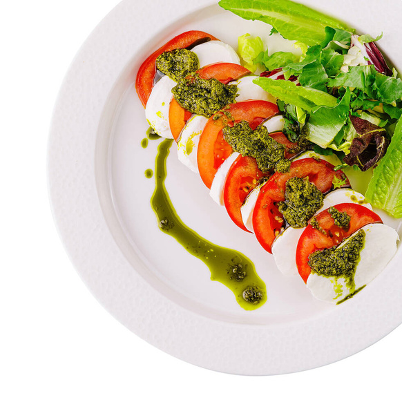 Visão aérea da salada caprese com tomates maduros, mussarela, pesto de manjericão e verduras na placa branca - Foto, Imagem
