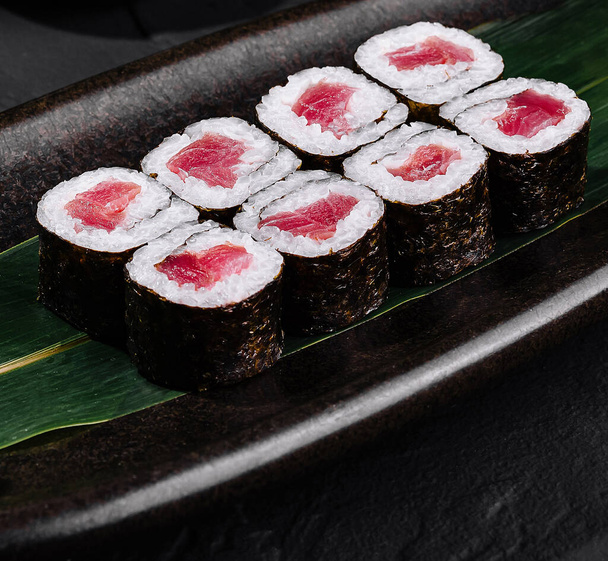 Rotolo di sushi al tonno splendidamente organizzato su una foglia, con zenzero e wasabi, su una superficie nera elegante - Foto, immagini