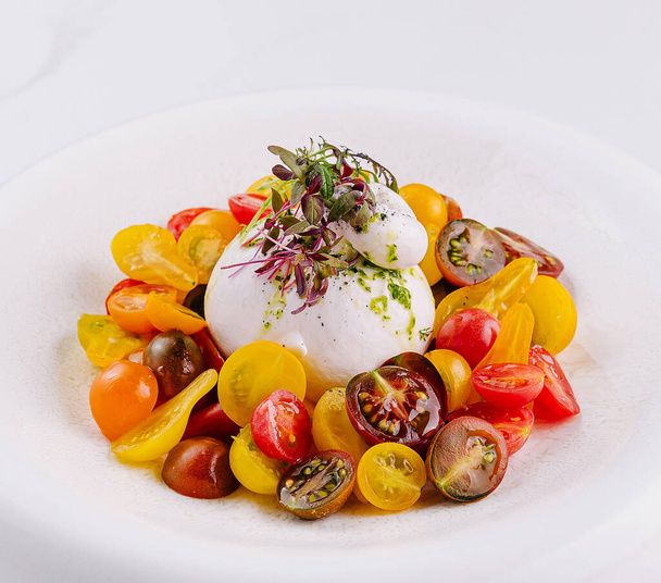 Burrata fresca com tomates cereja coloridos e ervas, apresentado em um prato branco, fundo de mármore - Foto, Imagem