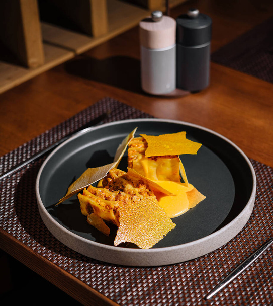 Искусно покрытые тыквенные равиоли с хрустящим шалфеем на современной темной тарелке в изысканном ресторане - Фото, изображение