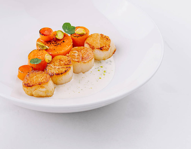 Vieiras doradas gourmet con hierbas y guarnición servidas en un plato blanco elegante - Foto, imagen