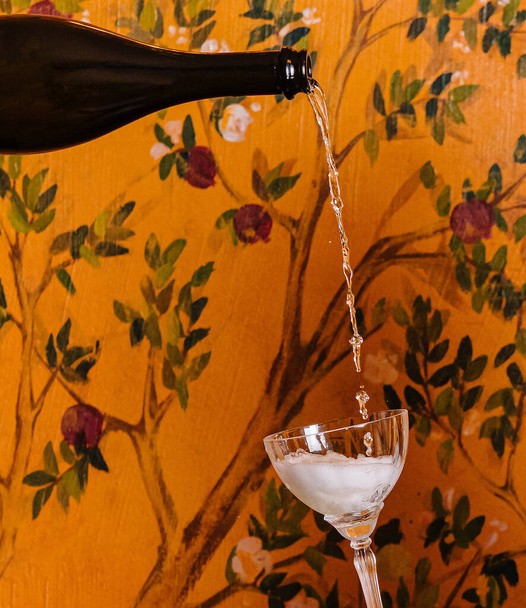 A személy pezsgőt önt egy üvegbe dekoratív virágos háttérrel - Fotó, kép