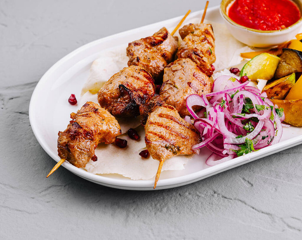 Skewered kebab eten met geroosterde groenten en pittige saus op een wit bord - Foto, afbeelding
