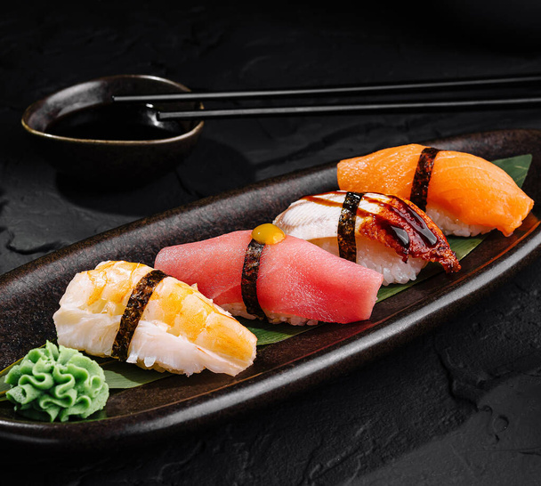 Finom nigiri sushi választék, fekete tálcán tálalva szójaszósszal és evőpálcikával. - Fotó, kép