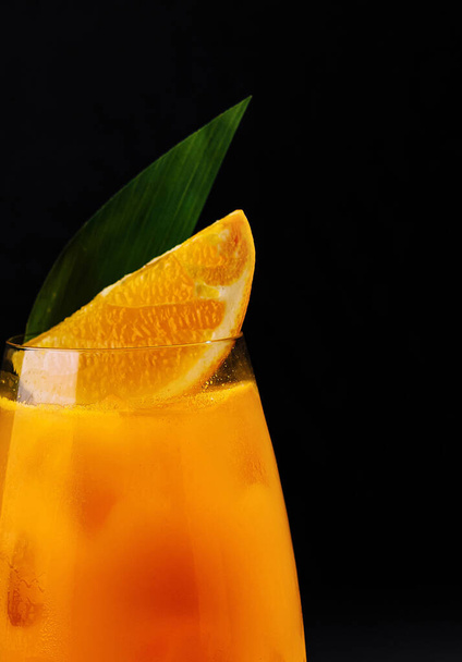 Živý pomerančový nápoj ve sklenici, zdobený plátkem a listem, na tmavém pozadí - Fotografie, Obrázek
