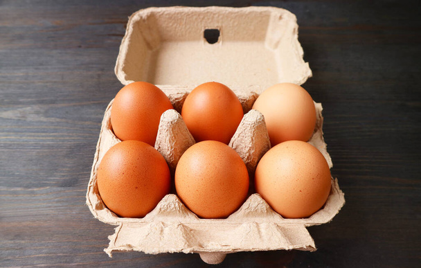 Органические куриные яйца в коробке из-под бумаги, изолированные на черном деревянном столе - Фото, изображение