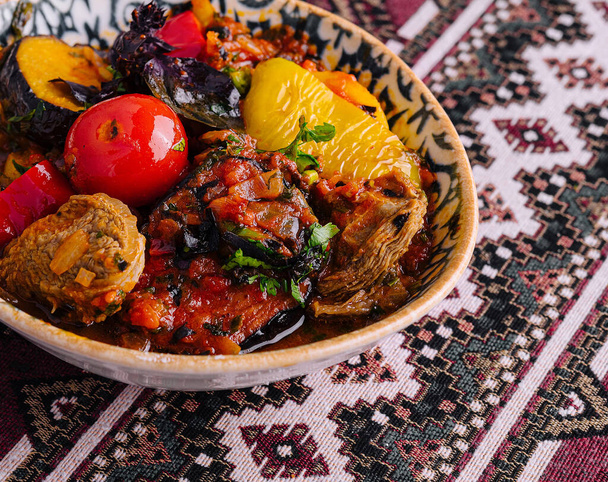 Ragoût d'uzbek salé aux légumes et herbes mélangés, servi dans un bol décoratif sur une nappe à motifs - Photo, image