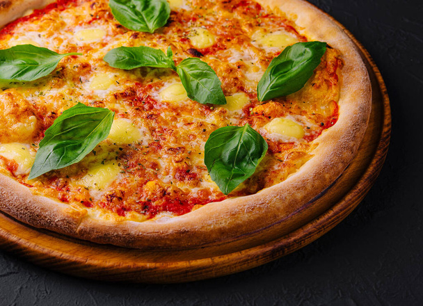 Pizza de margherita recién horneada con hojas de albahaca sobre un fondo de textura oscura - Foto, Imagen