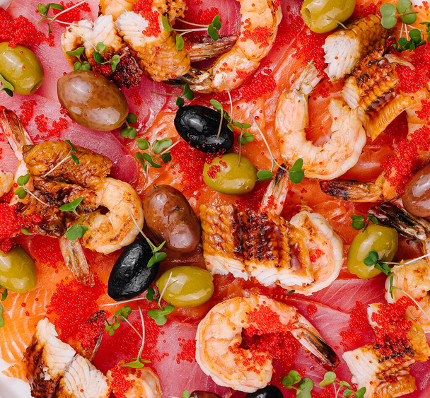 Vista dall'alto di un delizioso piatto di pesce gourmet con gamberi, caviale e olive su un piatto vibrante - Foto, immagini