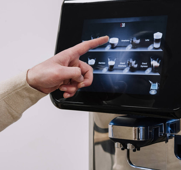 Persoon met behulp van een vinger om opties te selecteren op een geavanceerde koffiezetapparaat touchscreen display - Foto, afbeelding