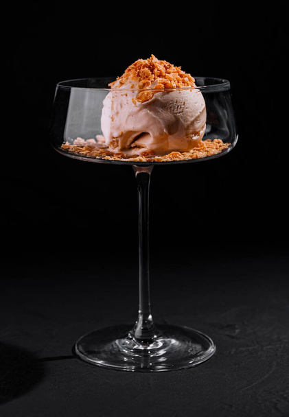 Postre de helado ingeniosamente plateado con cobertura desmenuzada en un elegante vaso coupé sobre un fondo oscuro - Foto, Imagen