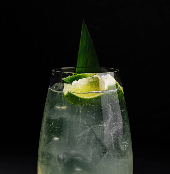 Elegant glas limoencocktail met ijsblokjes en groene bladgarnering, geïsoleerd op donkere achtergrond - Foto, afbeelding
