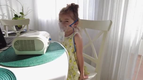 Cute little girl in the mask of an inhaler. Procedure of inhalation at home. Kid taking respiratory therapy with nebulizer. - Footage, Video