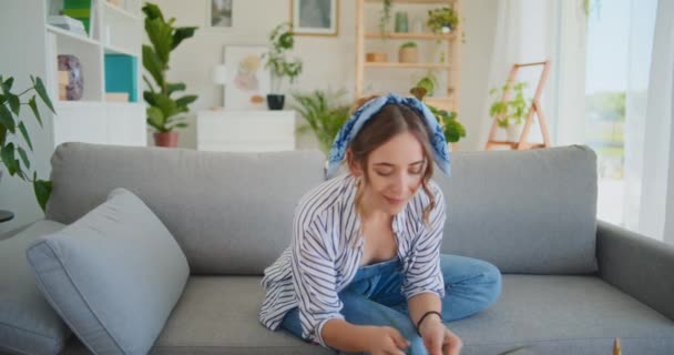 With a joyful smile, a woman basks in happiness after successful online shopping on her smartphone while lounging comfortably on the sofa - Footage, Video