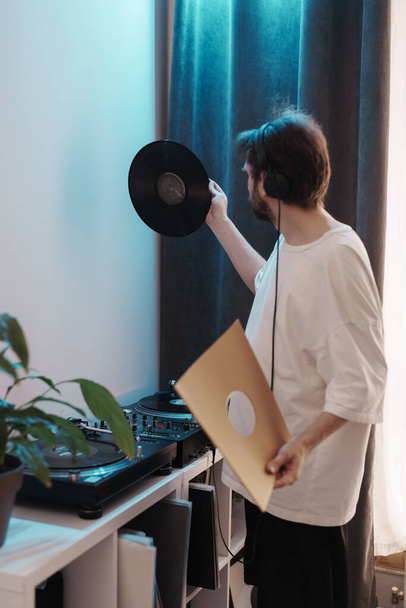 Audiofil se sluchátky zkoumajícími vinylovou desku uvnitř. Koncept domácí zábavy. - Fotografie, Obrázek