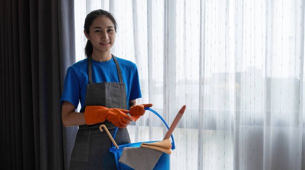 Una giovane donna di pulizia si alza in piedi tenendo gli strumenti di pulizia e si prepara a pulire il pavimento.. - Foto, immagini