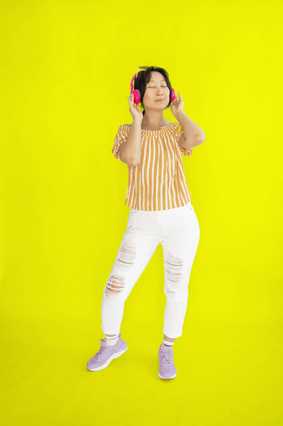 volledige lengte lichaam grootte foto van dansen aziatisch meisje verbeelden zich op disco terwijl geïsoleerd op gele achtergrond. - Foto, afbeelding