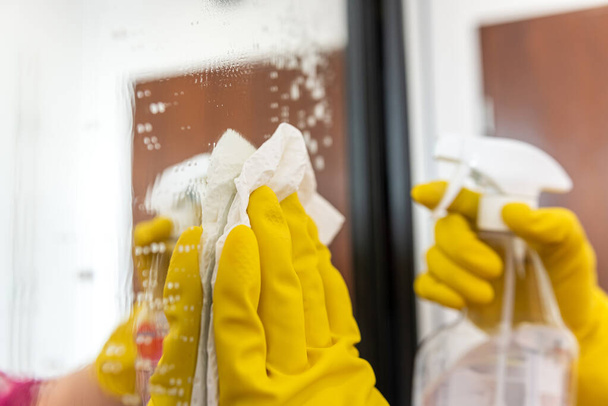 Kadın eldiven takıyor ve evdeki gardıroba cam siliyor. Evdeki temizlikçi.. - Fotoğraf, Görsel
